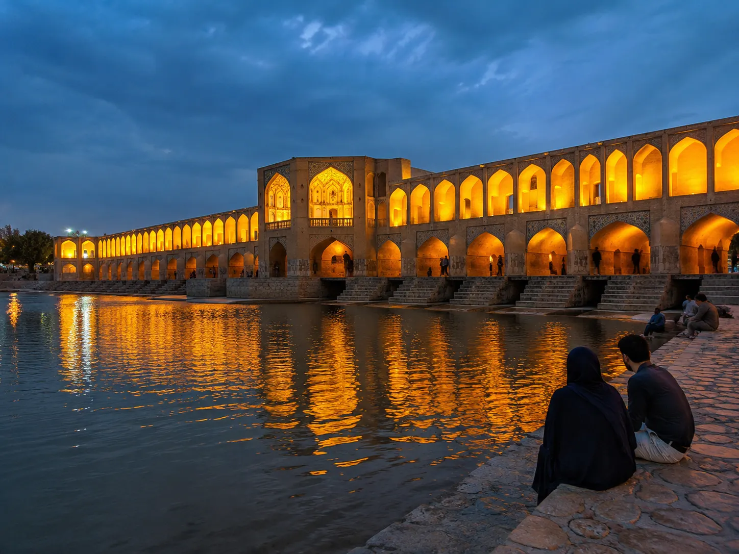 Historic Si-o-se-pol bridge illuminated at night reflecting on river water in Isfahan