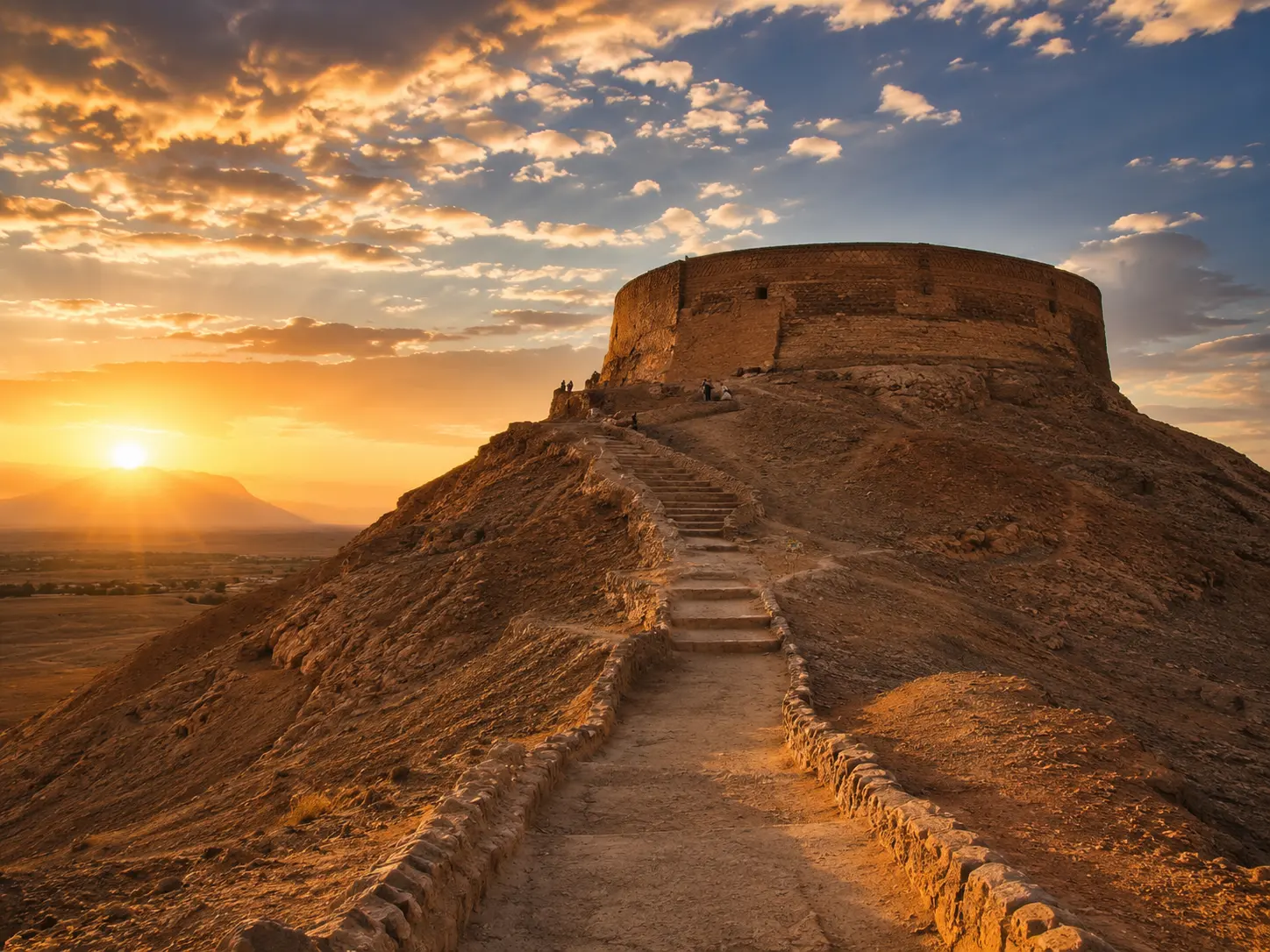 Narin Castle near Yazd at sunset with desert hill, stone path, and golden sky